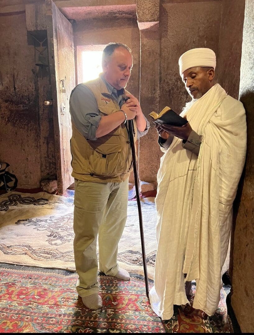 A man standing next to another man in white robes.